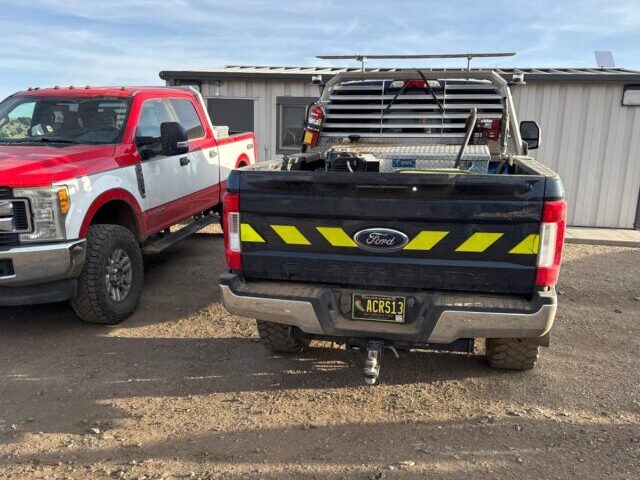 Black Ford F-250 Super Duty work truck with fluorescent yellow and black reflective chevron stripes across the tailgate, parked at a job site.