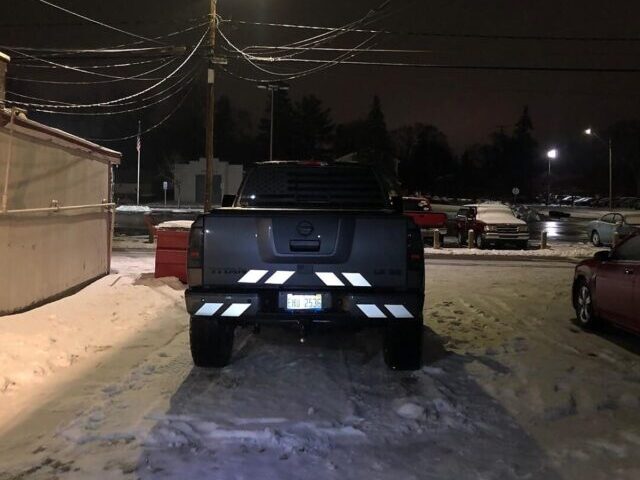 Gray Nissan Titan pickup truck rear view at night in snowy conditions, with white reflective shadow chevron stripes brightly reflecting on the tailgate and bumper.