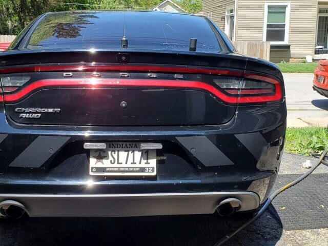 Black Dodge Charger AWD rear view with gray reflective shadow chevron stripes on the lower bumper, law enforcement vehicle parked in a residential driveway.